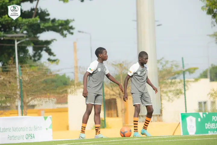 Deux jeunes joueurs sur le terrain, devant une banderole de la Loterie Nationale du Bénin